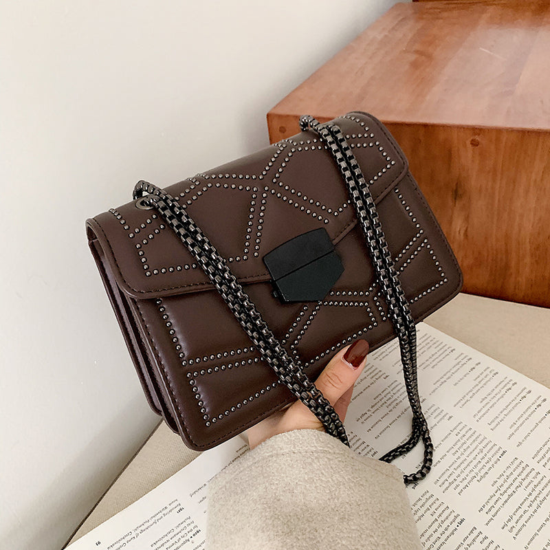 Black chain shoulder messenger bag for women displayed with stylish studs and a lock closure on a table.