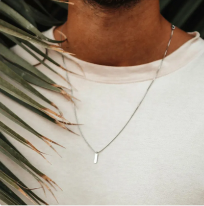 Model wearing a stainless steel clavicle chain necklace with a sleek pendant, enhancing casual style against tropical leaves.