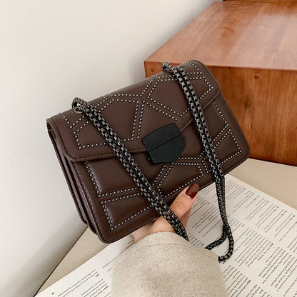 Black chain shoulder messenger bag for women displayed with stylish studs and a lock closure on a table.