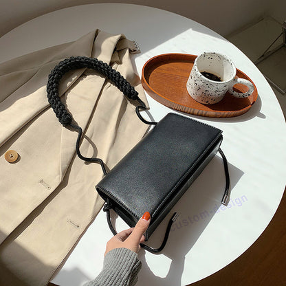 Black small square messenger bag on a table beside a cup, showcasing its chic design and functional style.